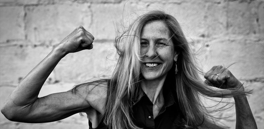 Fotografía de la escritora estadounidense Bonnie Jo Campbell en actitud triunfadora mostrando la musculatura de sus brazos mientras sonríe con el pelo revuelto.